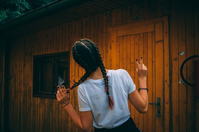 Žena so zapletenými vrkočmi stojí pred nízko podlažným domčekom